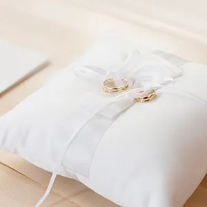 Anillos dorados sobre coj&iacute;n blanco de boda con cintas