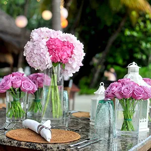 Arreglo de flores rosas en mesa con frascos y lanternas blancas