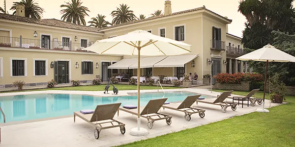 Piscina y jardines con tumbonas y sombrillas junto a un edificio colonial.