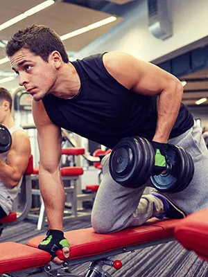 Hombre entrenando con mancuernas en banco en gimnasio.