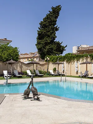 Piscina azul con dos estatuas y jard&iacute;n en un hotel bajo cielo despejado.