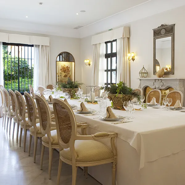 Comedor elegante con mesa vestida y sillas, iluminaci&oacute;n y decoraci&oacute;n.