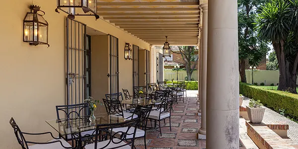 Pasillo con sillas y faroles junto a columnas, en patio ajardinado