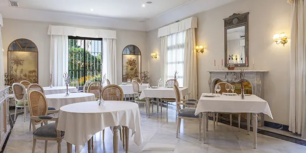 Comedor elegante con mesas, sillas y ventanas en un ambiente luminoso.