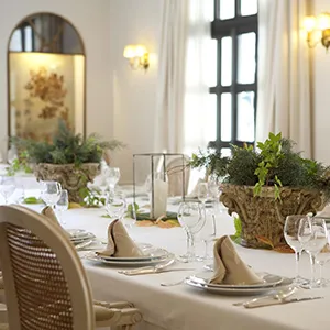Mesa de banquete con plantas y copas en un sal&oacute;n con ventanas