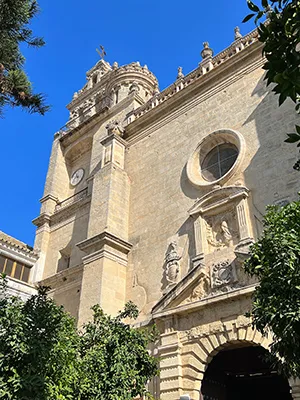 Fachada de una catedral hist&oacute;rica con c&uacute;pulas y reloj, entre &aacute;rboles