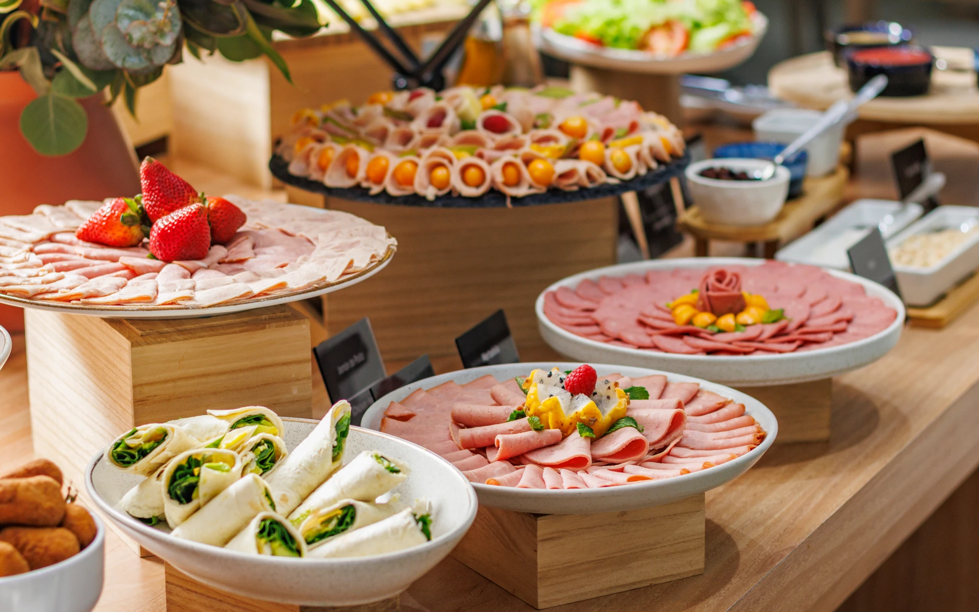 Buffet de embutidos y frutas con platos variados sobre una mesa de madera.