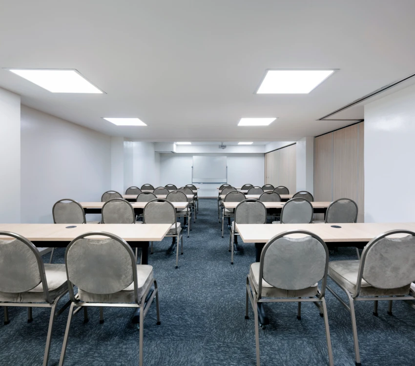 Aula vac&iacute;a con mesas, sillas grises y una pizarra blanca al fondo.