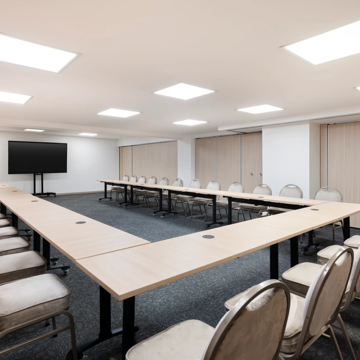 Sala de conferencias vac&iacute;a con mesas en forma de U y sillas alrededor.