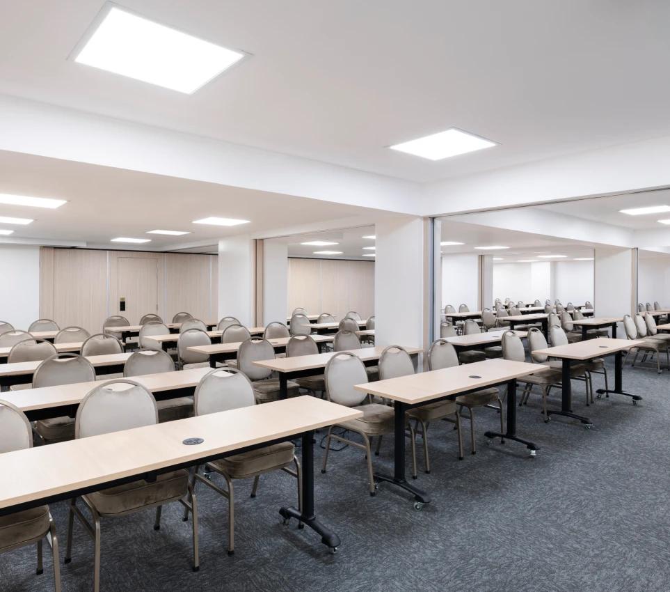 Sala de reuniones vac&iacute;a con mesas y sillas organizadas en filas.