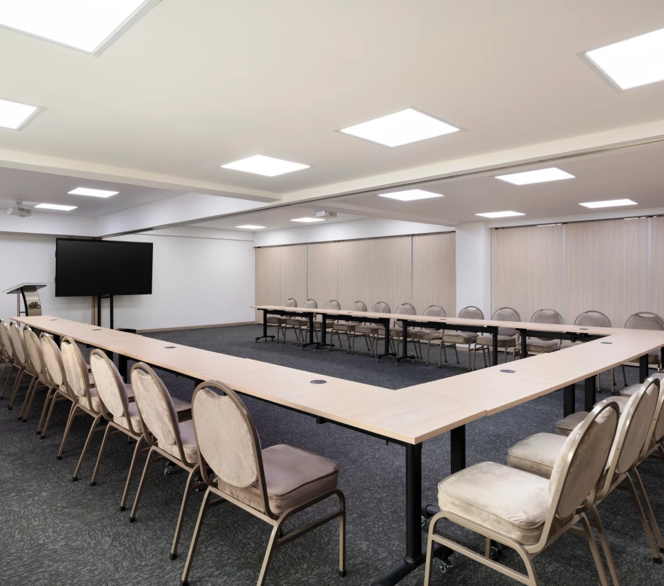 Sala de conferencias con mesas en forma de U y pantalla grande.