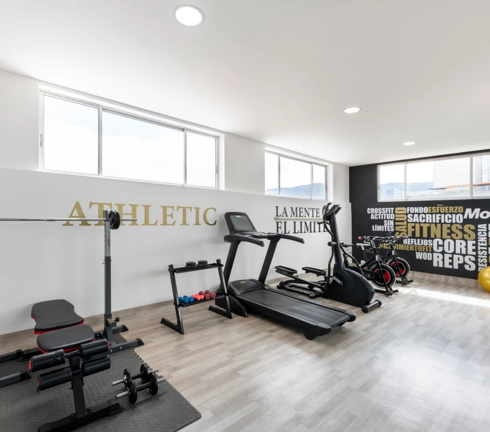 Gimnasio moderno con equipo de ejercicio y frases motivacionales en la pared.