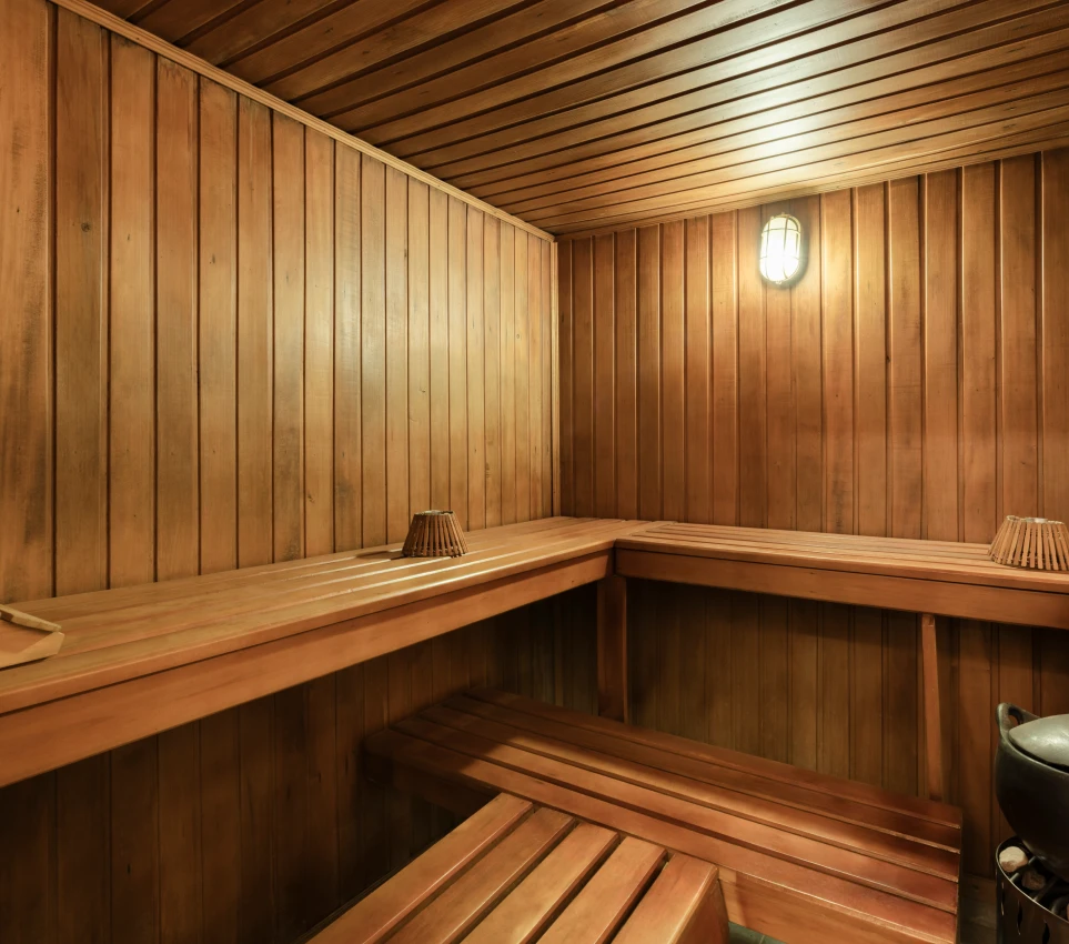 Interior de una sauna de madera con bancos y luz encendida.
