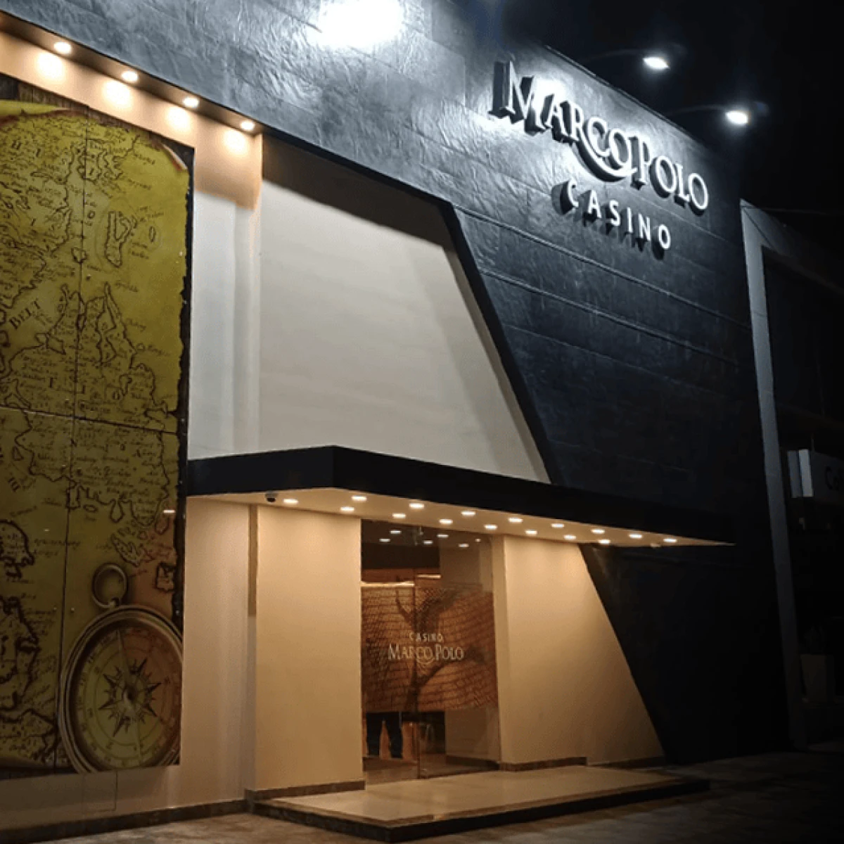 Fachada del casino Marco Polo iluminada de noche con un mapa antiguo decorativo.