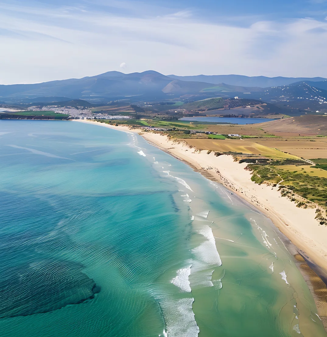 Costa con playa de arena blanca junto a monta&ntilde;as y mar turquesa.