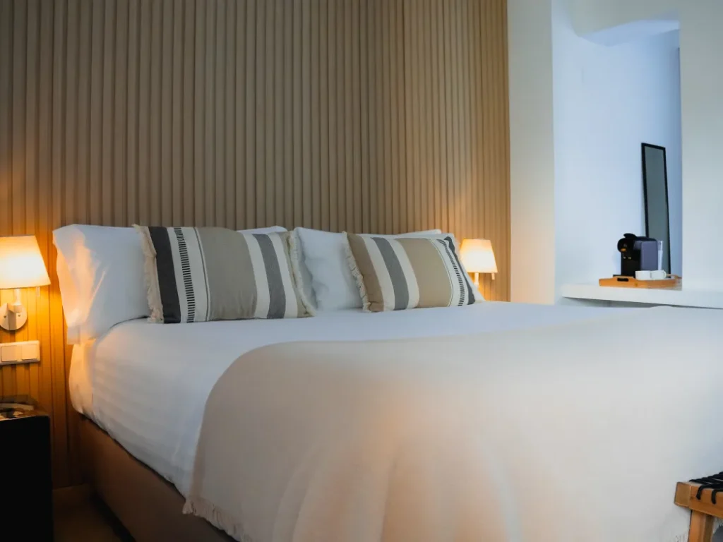 Dormitorio moderno con cama blanca, cojines a rayas y l&aacute;mparas de noche