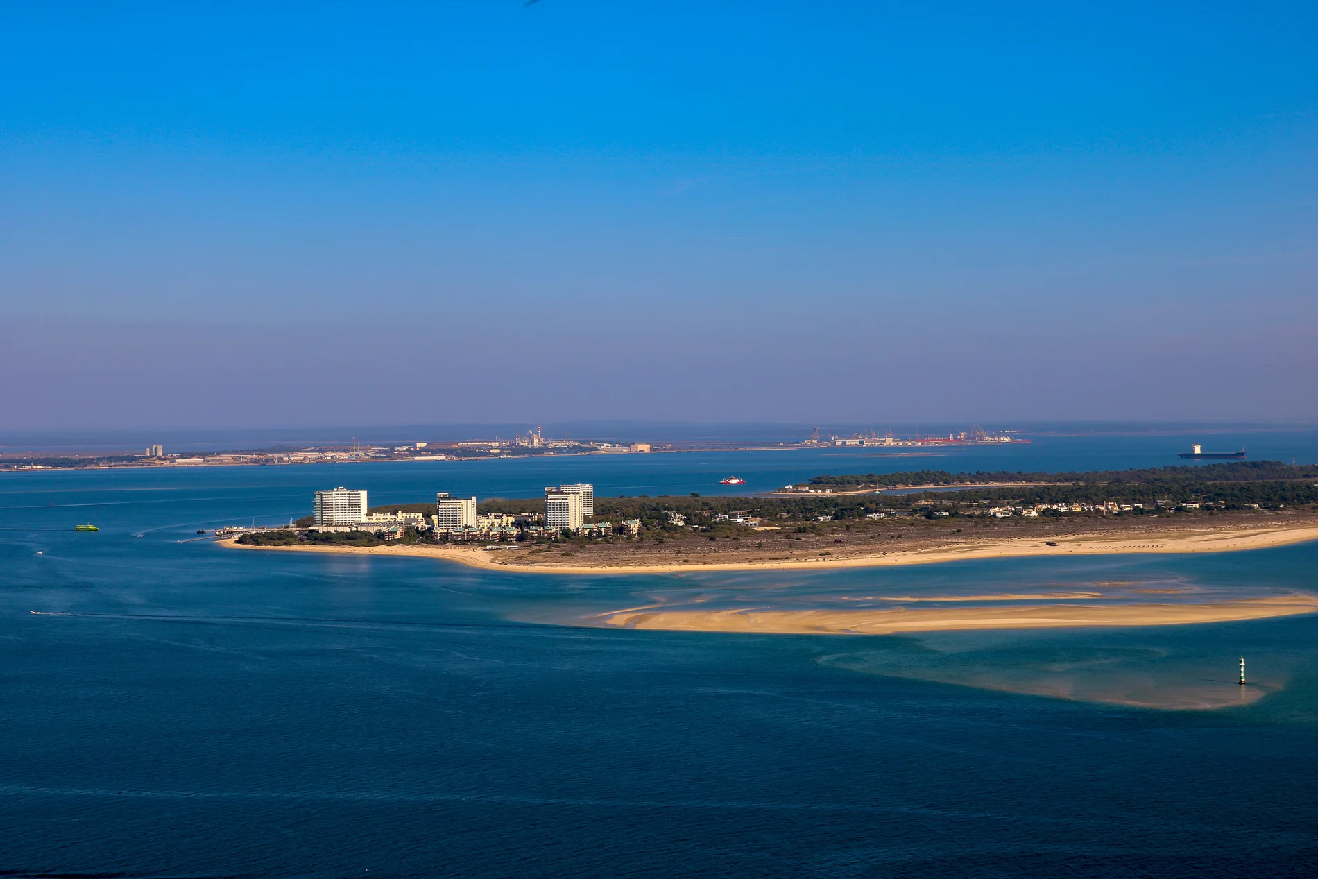 Vista a&eacute;rea de uma praia com pr&eacute;dios e mar azul ao fundo.
