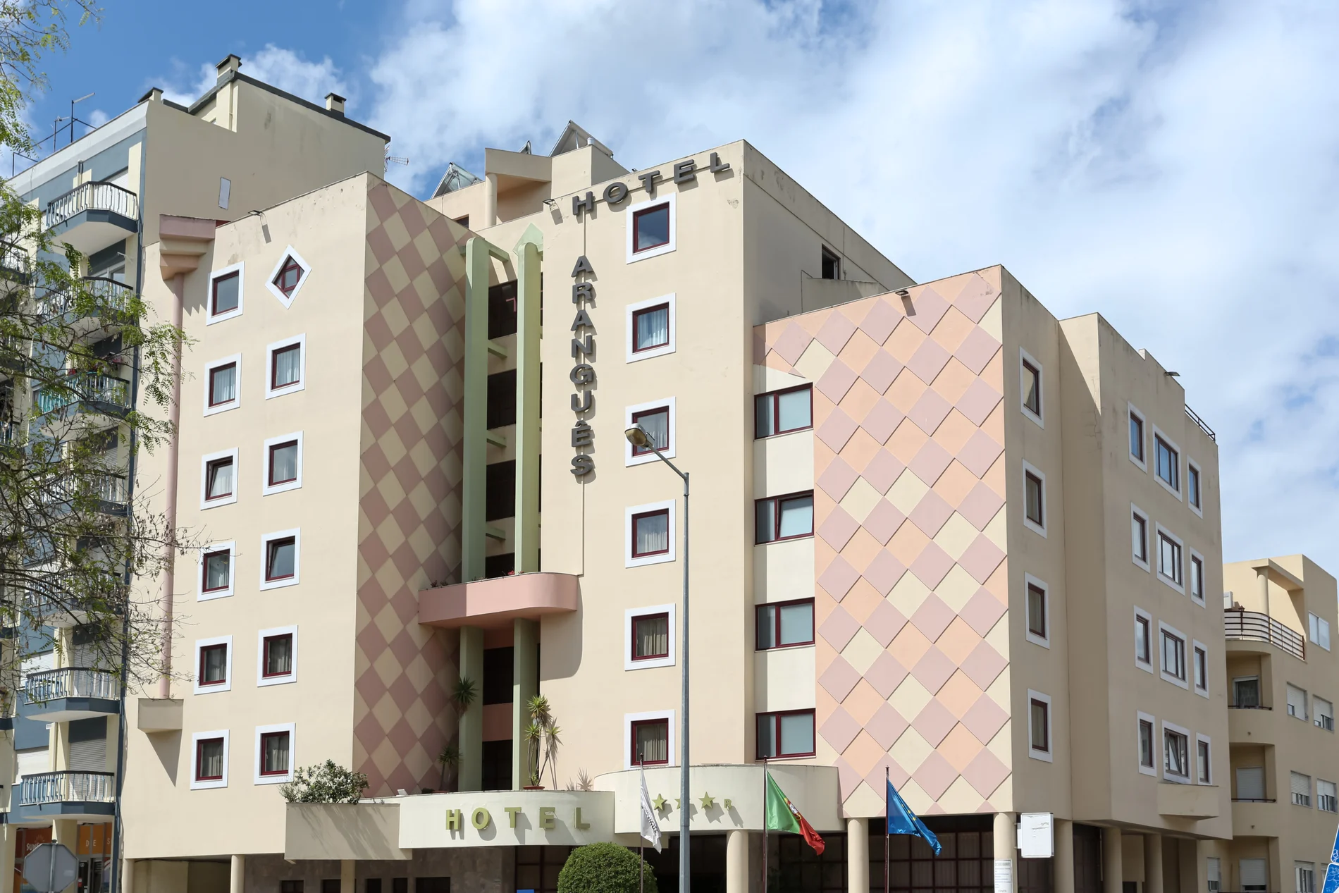 Fachada de um hotel com design geom&eacute;trico e bandeiras na entrada.