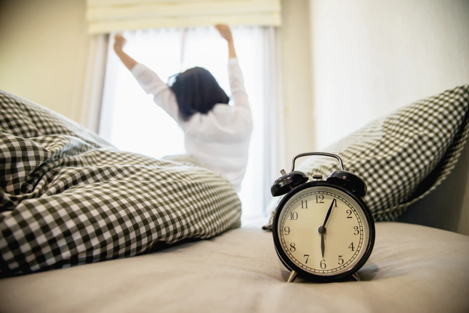 Despertador no primeiro plano e pessoa se espregui&ccedil;ando ao fundo.