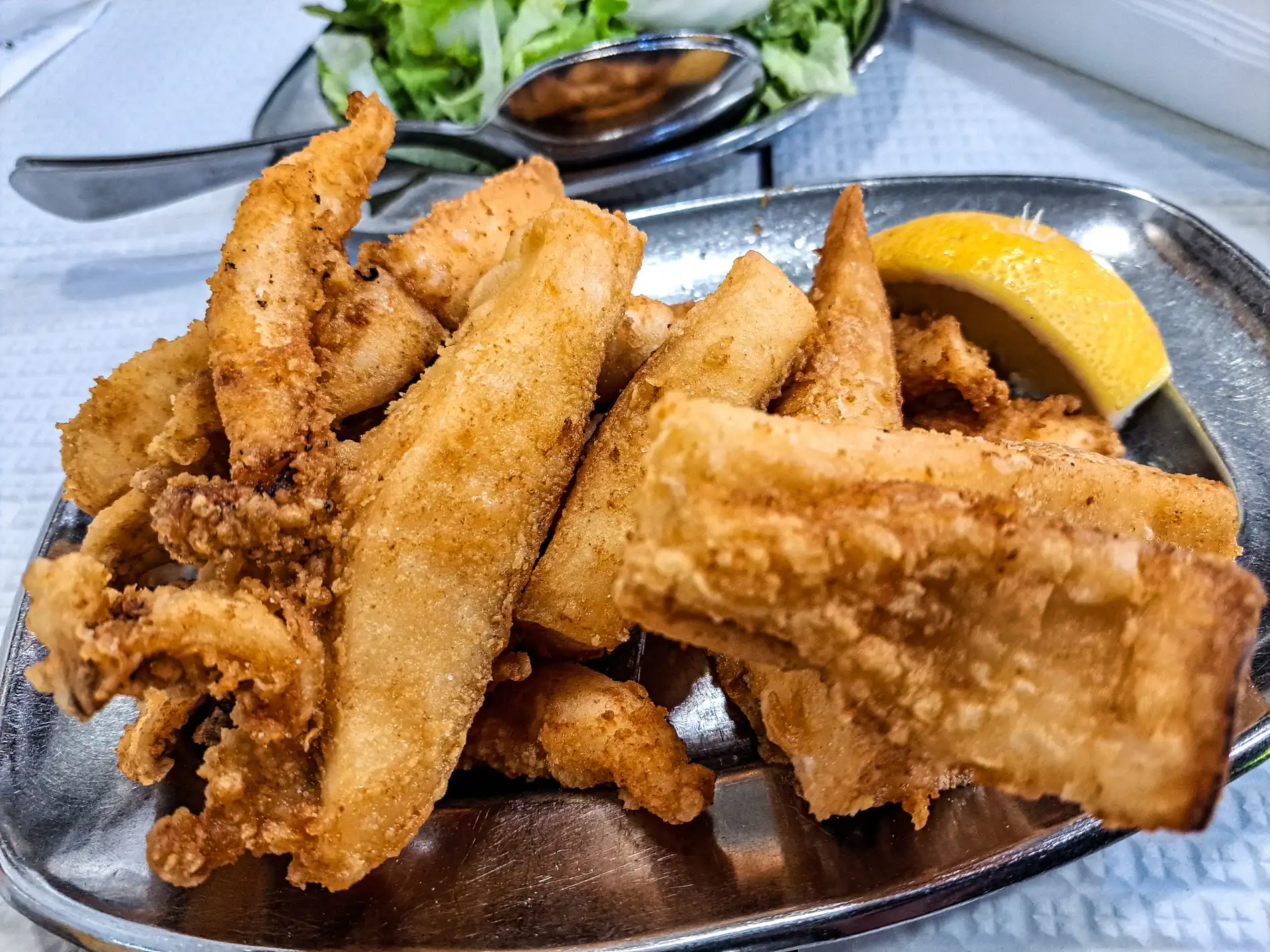 Lula frita com lim&atilde;o em prato de metal, salada ao fundo.