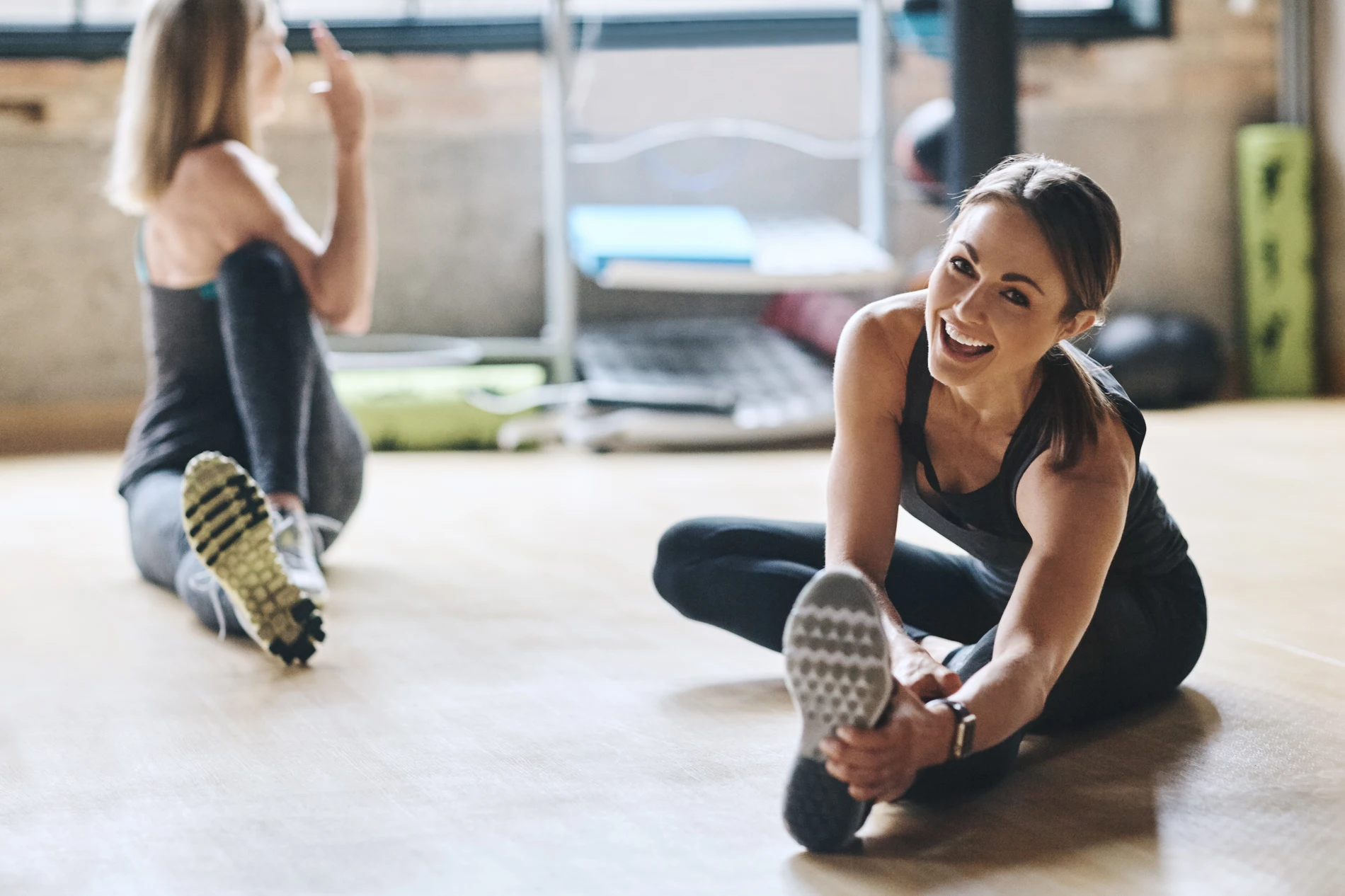 Duas mulheres se alongando em uma aula de exerc&iacute;cio f&iacute;sico em academia.