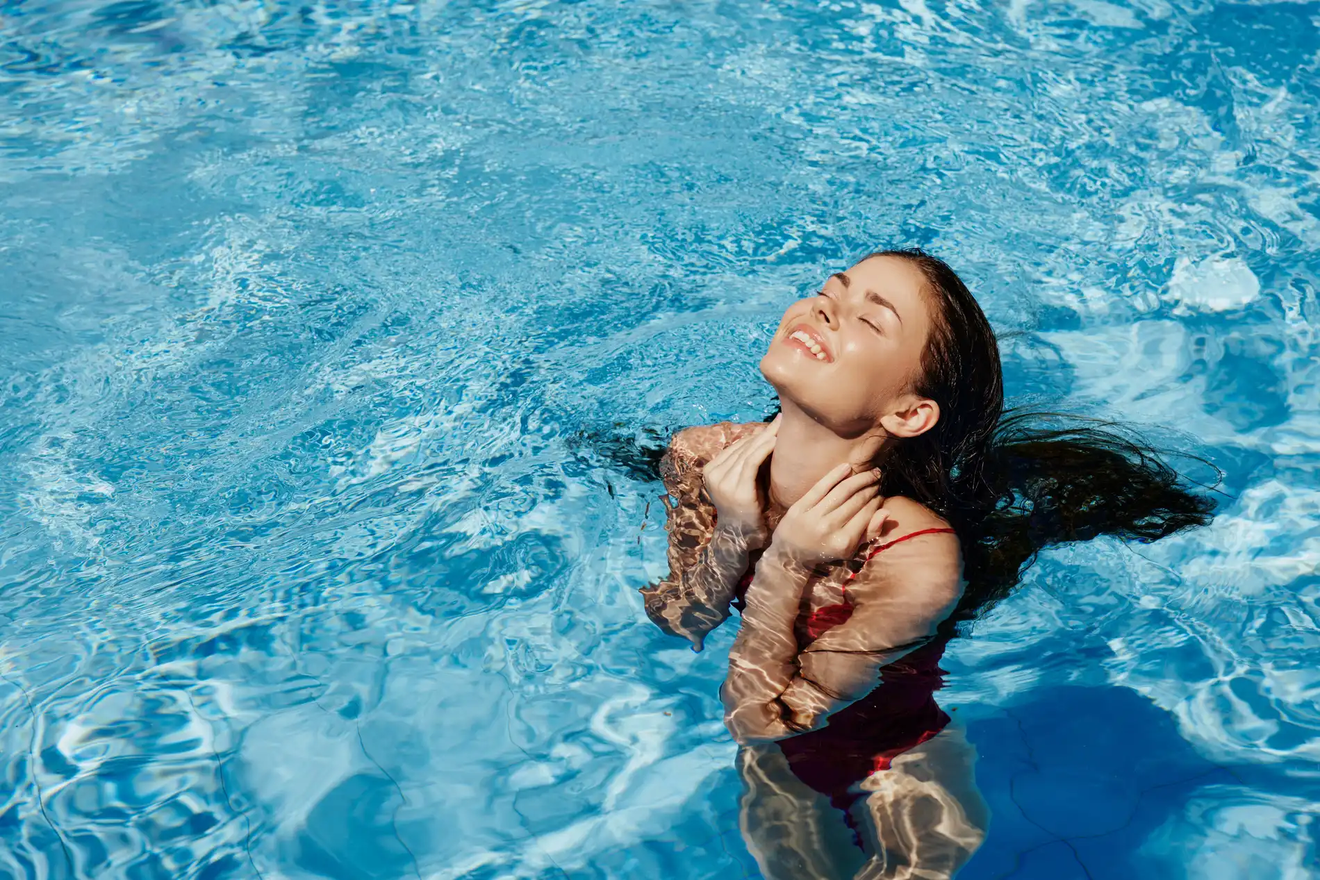 Mulher sorrindo e relaxando em uma piscina azul clara.