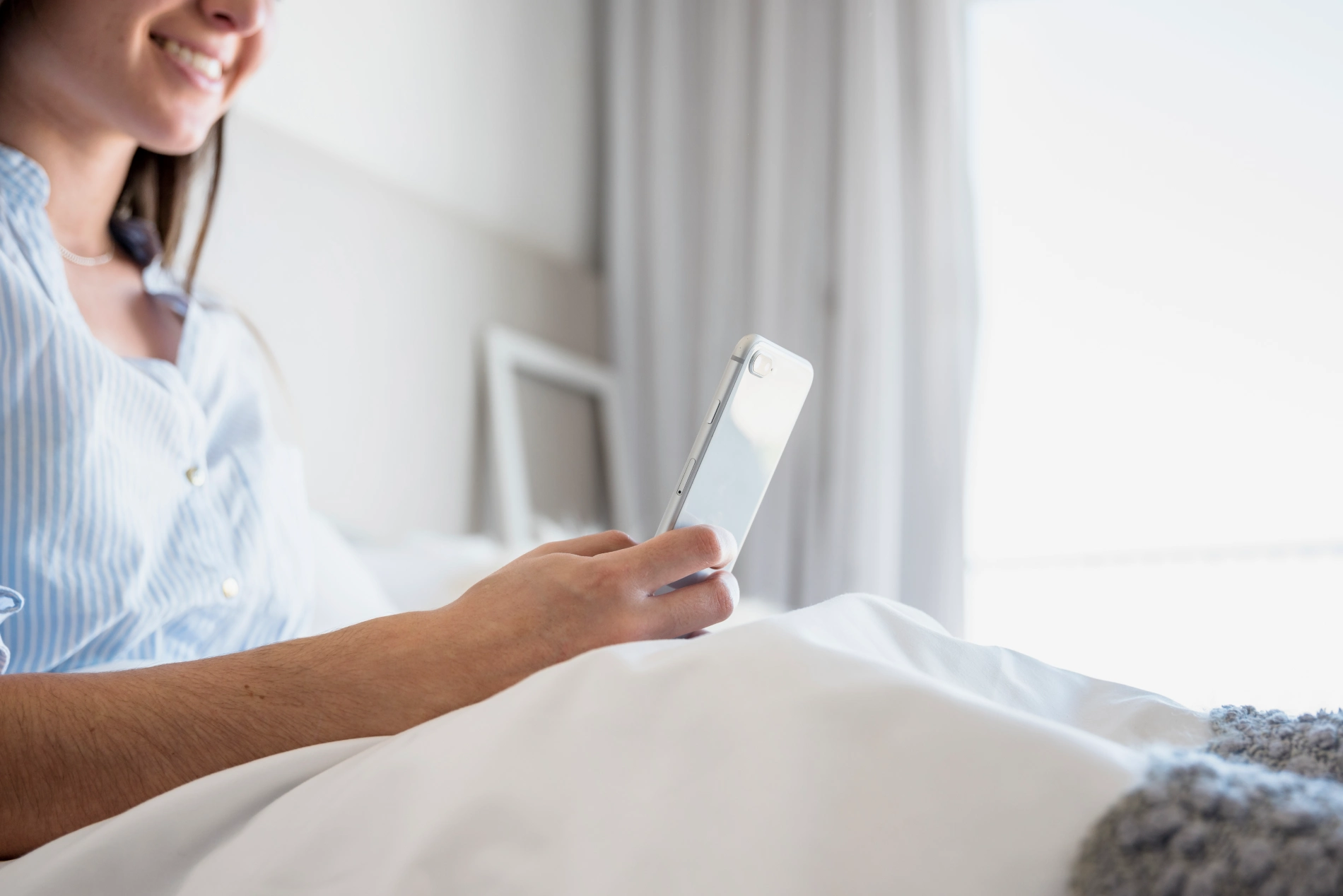 Pessoa sorrindo enquanto usa o celular na cama.