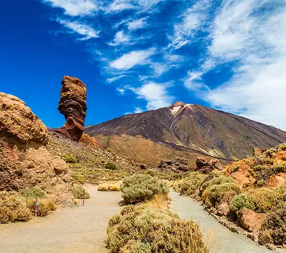 Rocky landscape with a towering rock and mountain under a blue sky.
