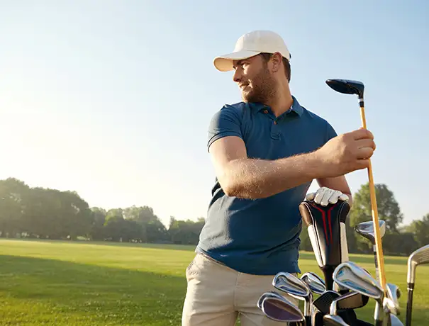 Golfer selecting a club from a bag on a sunny course.