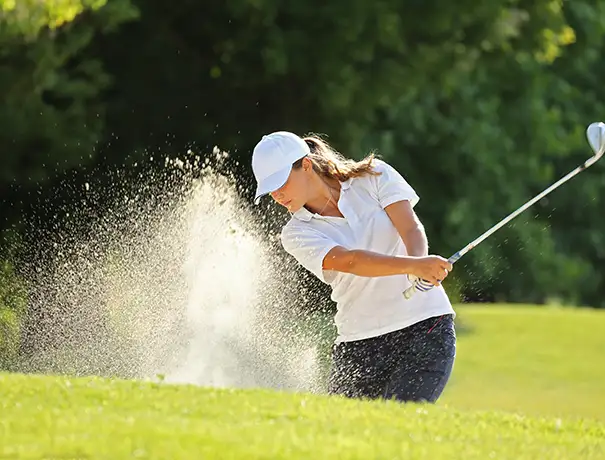 Golfer hitting ball from sand trap, creating a spray of sand.