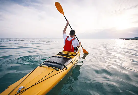 Person kayaking on calm sea at sunset.