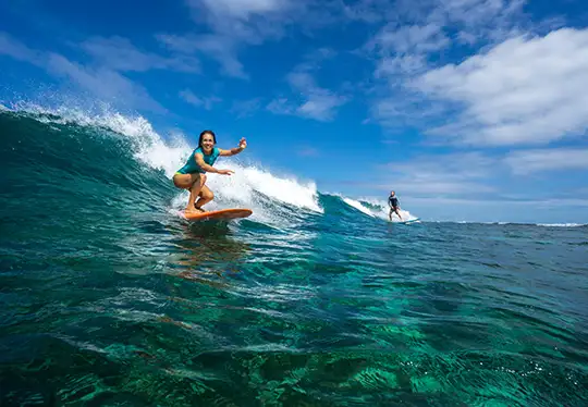 Two surfers ride waves under a clear blue sky.