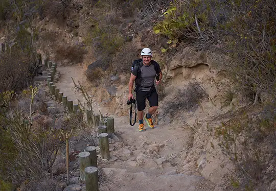 Person hiking uphill on a rocky trail with backpack and helmet.