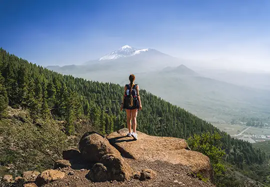 Hiker on a cliff with a snowy mountain view in the background.