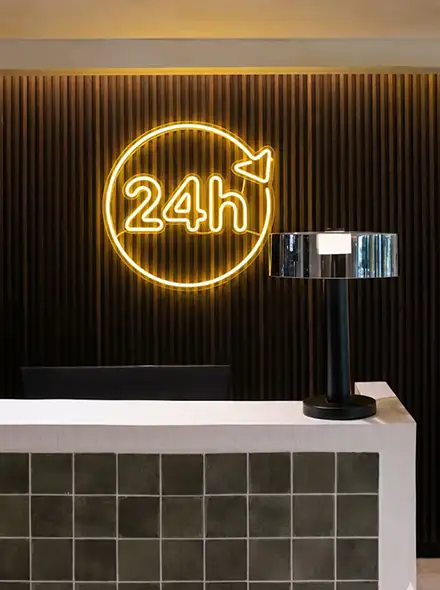 Reception desk with a neon "24h" sign and a black lamp.