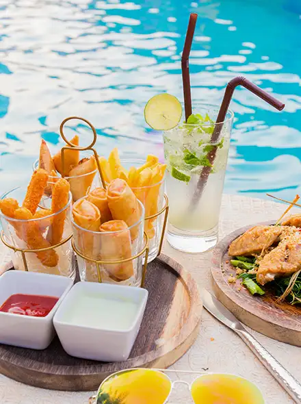 Snacks and drinks by a poolside with colorful sunglasses and sauces.