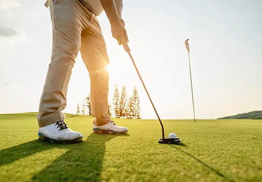 Golfer putting with sun setting behind, aiming for the hole.