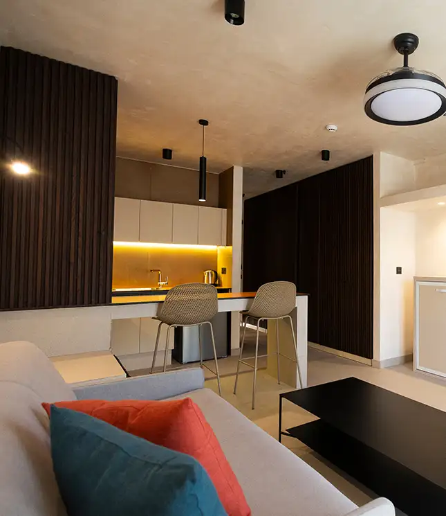 Modern kitchen and living area with bar stools, sofa, and colorful cushions.