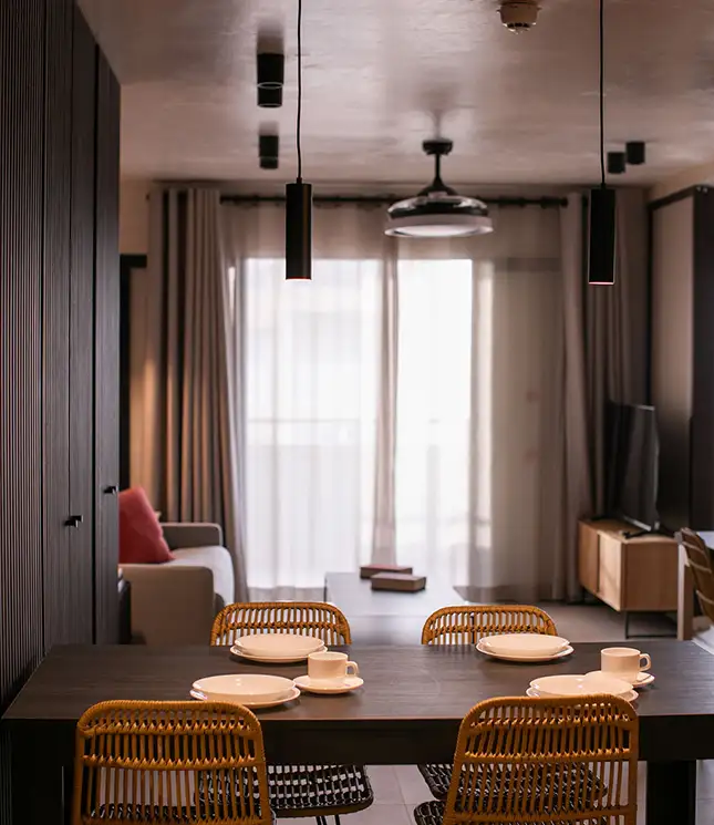 Modern dining area with a dark table, wicker chairs, and pendant lights.