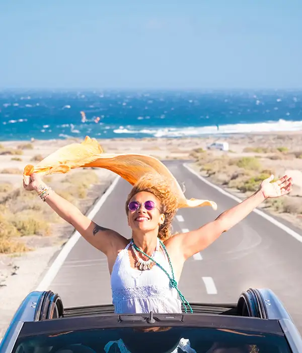 Woman enjoying a convertible ride by the sea, arms outstretched.