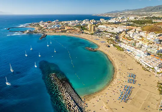Aerial view of a coastal city with sandy beaches and boats in the blue sea.