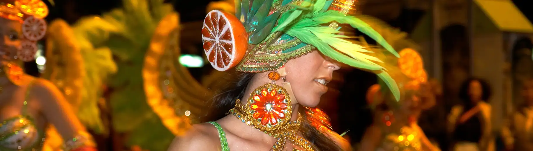Carnival dancer in vibrant costume with feathers and citrus decorations.