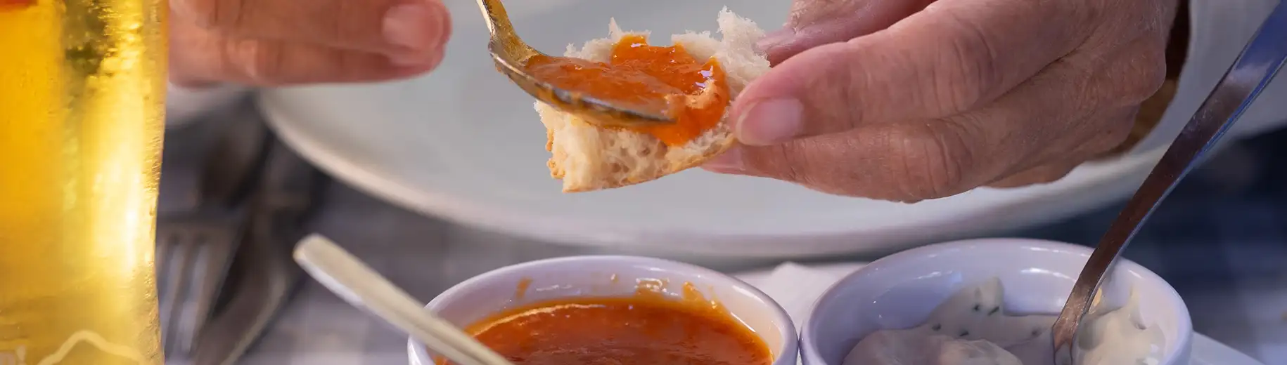 Hand spreading orange sauce on bread near two small bowls.