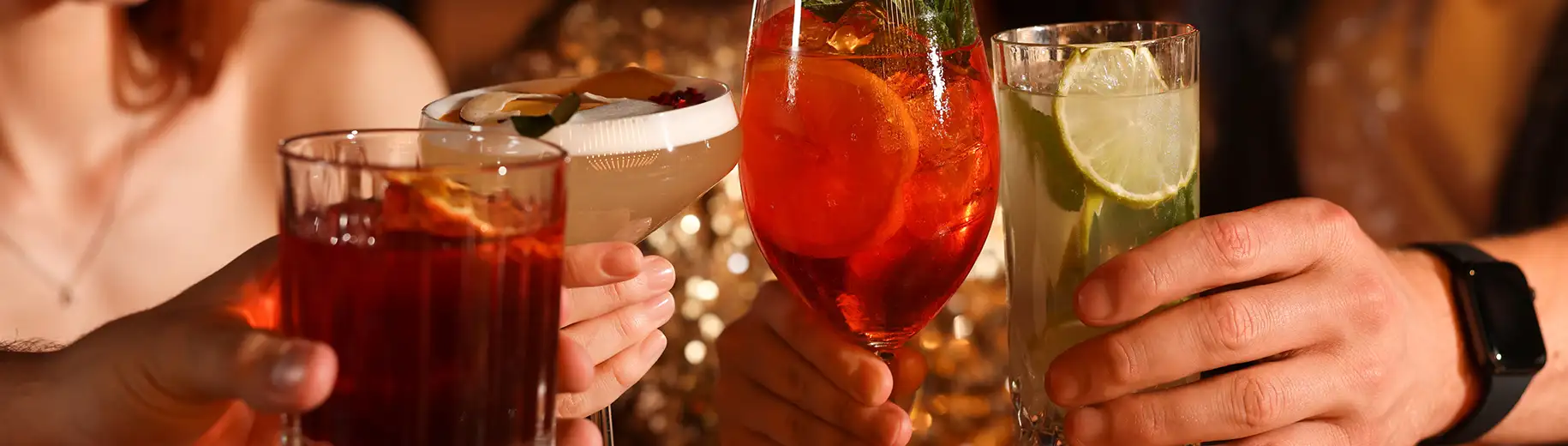 Hands toasting with colorful cocktails in glasses.