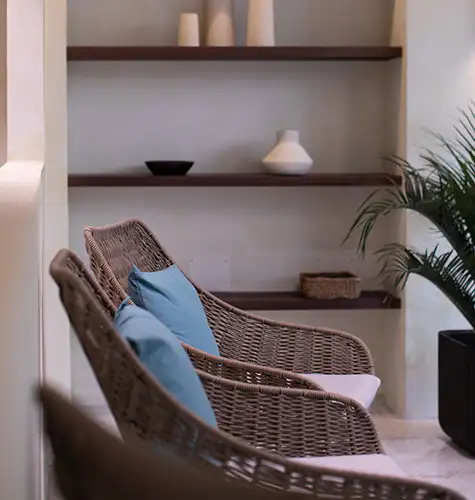 Wicker chairs with blue cushions beside shelves and a plant.