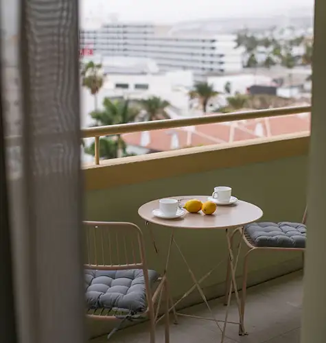 Balcony table with two cups and lemons, overlooking a cityscape.