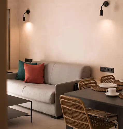 Cozy living room with a sofa, pillows, and dining table set in warm lighting.