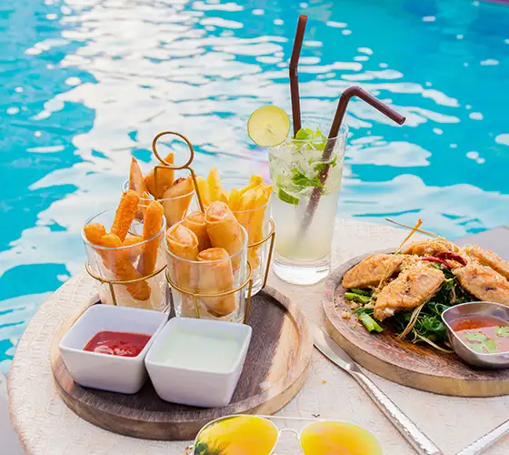 Snacks and drink by a poolside with dip sauces and grilled skewers.