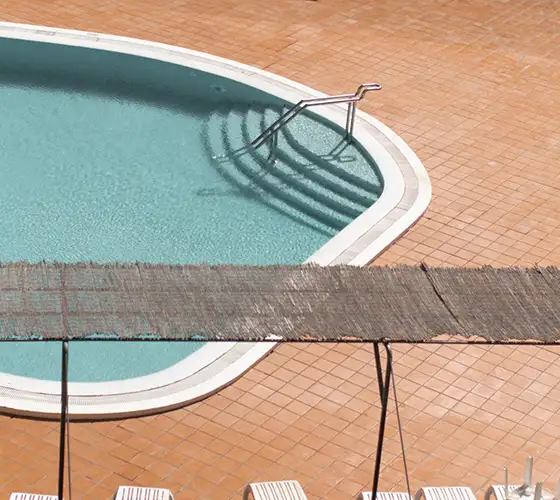 Small pool with orange tile deck, shadowed stairs, and a thatched awning above.