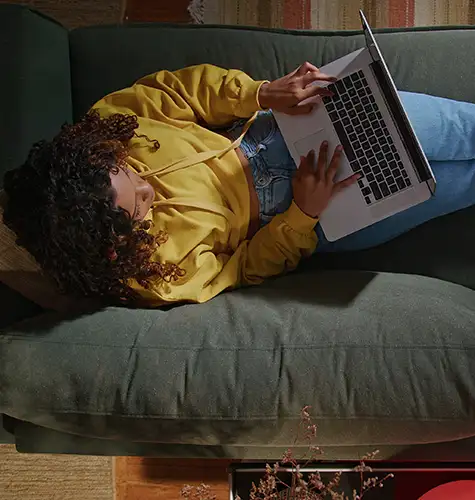 Person lying on a sofa working on a laptop.